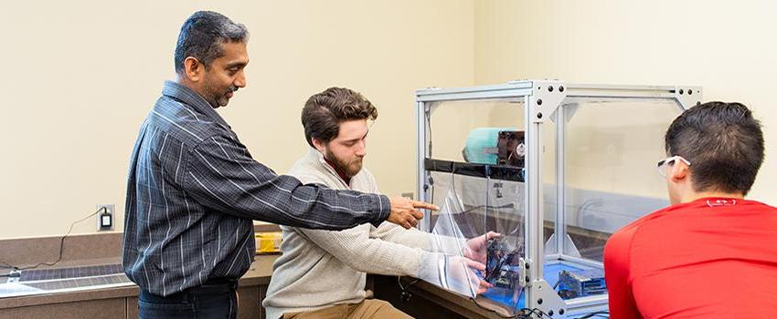 电气工程 Professor pointing at machine students are working on.