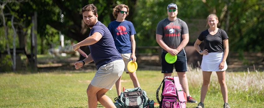 学生 playing disc golf on campus with club sports.